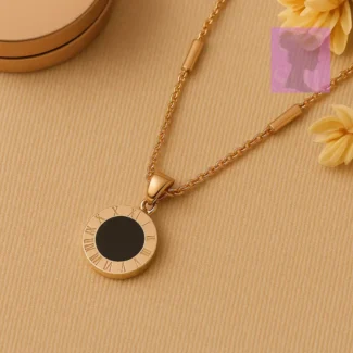Gold Roman numeral necklace with black center placed near soft-focus yellow flowers on a beige surface
